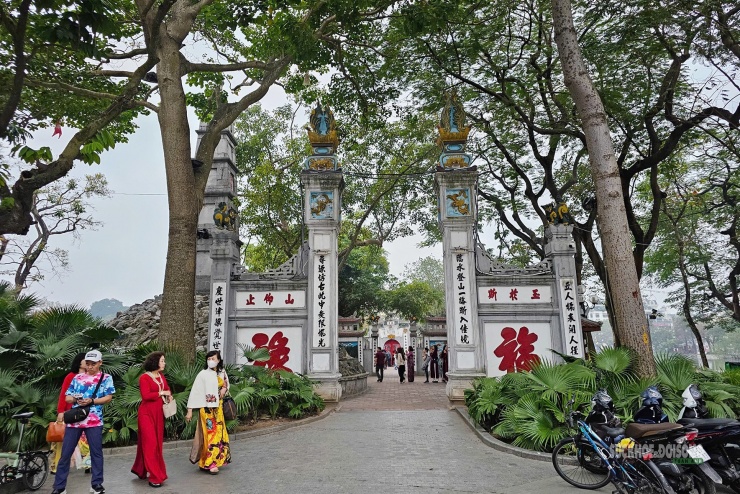 Du khách du xuân qua cổng đền Ngọc Sơn sáng mồng Một Tết, giữa không gian xanh mát và nhịp bước thong dong ngày đầu năm mới.