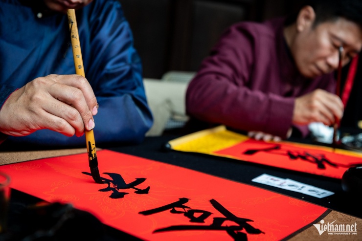 Một ông đồ đang viết những nét chữ cứng cáp lên tờ giấy đỏ.