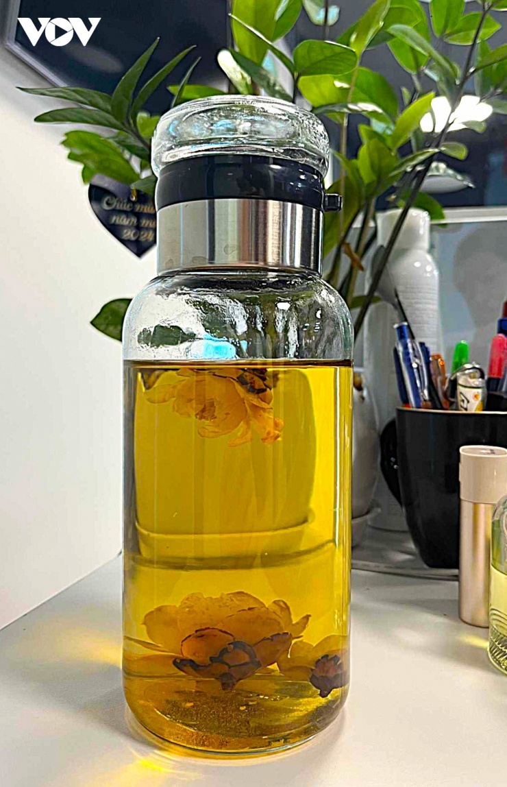 Bình đựng trà hoa vàng đã pha sẵn từ nhà mang tới công sở của chị Nga, trú ở Hà Nội. “Trà sau khi pha có màu nước vàng óng, vị thơm đặc trưng, dễ uống..”, chị Nga nhận xét. Theo một số tài liệu, tác dụng của trà này là hỗ trợ ổn định huyết áp và bảo vệ tim mạch, giải độc cơ thể, hỗ trợ điều hòa đường huyết, thanh lọc cơ thể, hỗ trợ giảm cân…(Ảnh: Hải Chi).