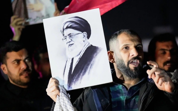 Ngày 28/2/2026, tại một cây cầu dẫn đến Khu vực Xanh được bảo vệ nghiêm ngặt, nơi đặt Đại sứ quán Mỹ ở Baghdad, Iraq, một người biểu tình cầm bức chân dung của Lãnh tụ Tối cao Iran Ali Khamenei trong cuộc biểu tình phản đối các cuộc tấn công của Mỹ và Israel nhằm vào Iran. Ảnh: AP.