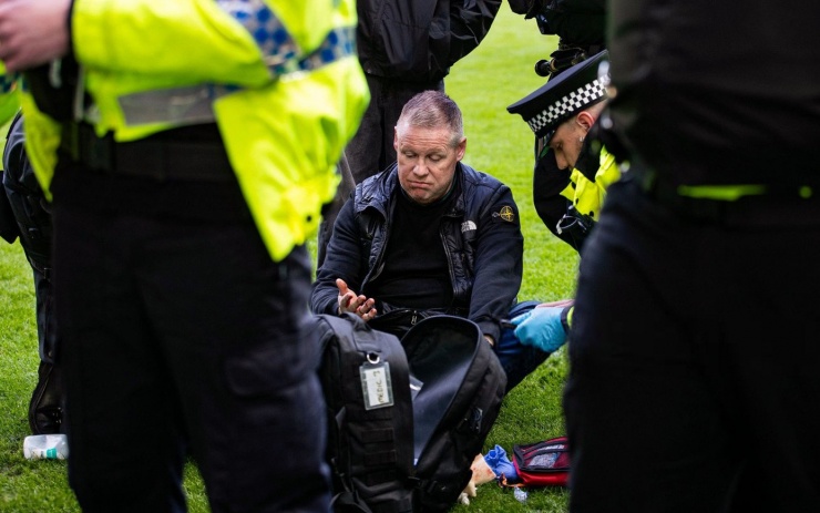 Một CĐV đổ máu sau cuộc đụng độ. Anh được nhân viên an ninh đứng vòng tròn để bảo vệ, đồng thời được nhân viên y tế chăm sóc.