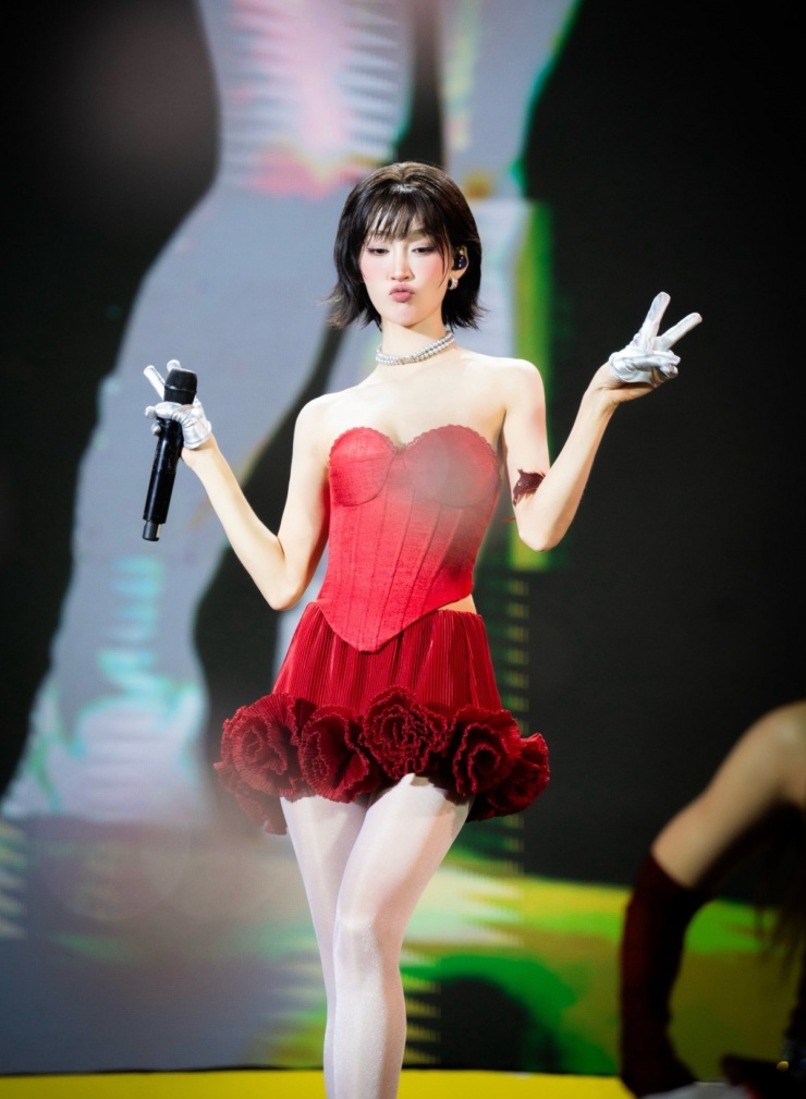 Trên sân khấu, Juky San thường chọn những trang phục có màu sắc nổi bật. Cô kết hợp corset đỏ rực với chân váy xếp ly 3D bắt mắt. Thiết kế corset với phần cúp ngực hình trái tim giúp tôn bờ vai và xương quai xanh, trong khi khoảng hở ở hông tạo điểm nhấn vào vòng eo, tăng vẻ gợi cảm khi cô thực hiện các động tác vũ đạo.