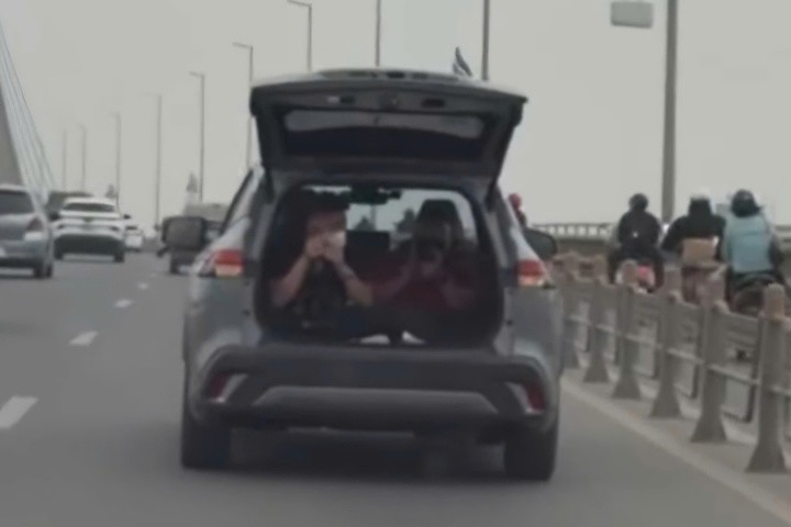 Hình ảnh hai người ngồi trong khoang hành lý phía sau chiếc ô tô mở cốp khi xe đang lưu thông trên cầu Nhật Tân, tiềm ẩn nguy cơ mất an toàn giao thông.