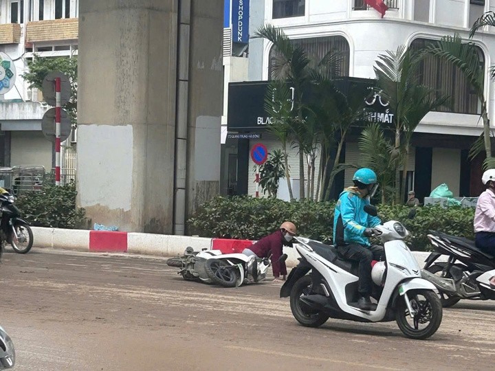 Người phụ nữ đi xe máy bị ngã ra đường do bùn đất trơn trượt.