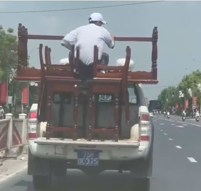 Chiếc xe bán tải chở bàn ghế cồng kềnh, phía trên còn có một người ngồi giữ lại. Ảnh cắt từ clip.