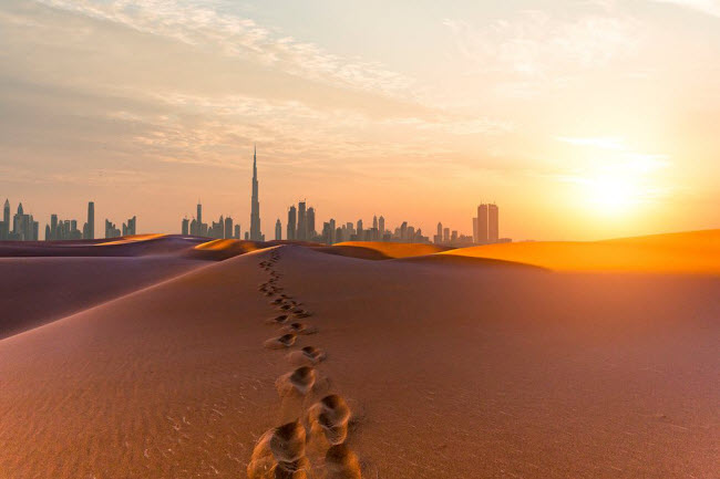 Dubai, UAE: Khung cảnh các tòa nhà cao chọc trời tại thành phố Dubai nhìn từ bề mặt cát màu cam trên sa mạc Ả Rập. Thành phố này nổi tiếng với các trung tâm mua sắm xa xỉ, kiến trúc hiện đại và cuộc sống ban đêm sôi động.
