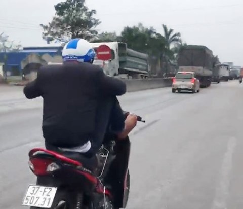 Nam thanh niên dùng 2 chân điều khiển xe máy, tay cầm điện thoại trên quốc lộ - 1