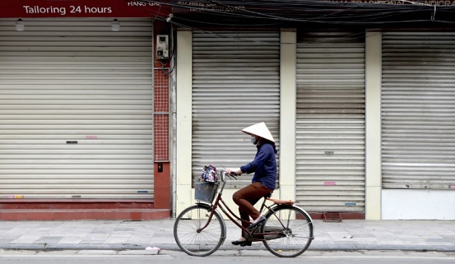 Người phụ nữ đạp xe trên đường phố vắng lặng ở Việt Nam. Ảnh: AP.