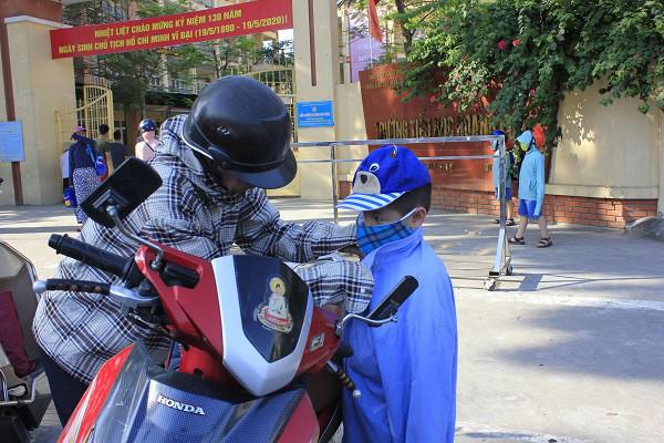 Con bước ra ngoài cổng trường được phụ huynh mặc áo khoác để chống nắng.