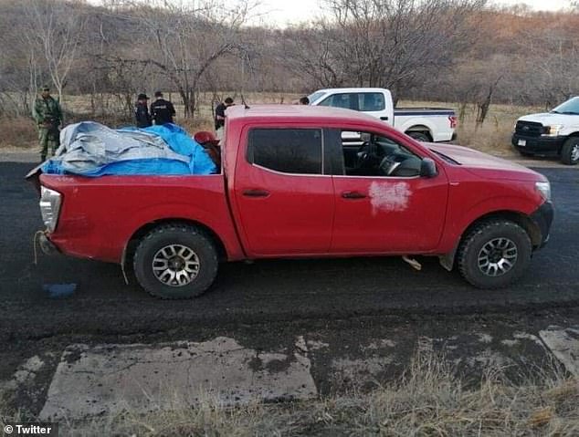 Chiếc xe bán tải màu đỏ bị bỏ lại trên đường, đã được phủ bạt để che các xác người