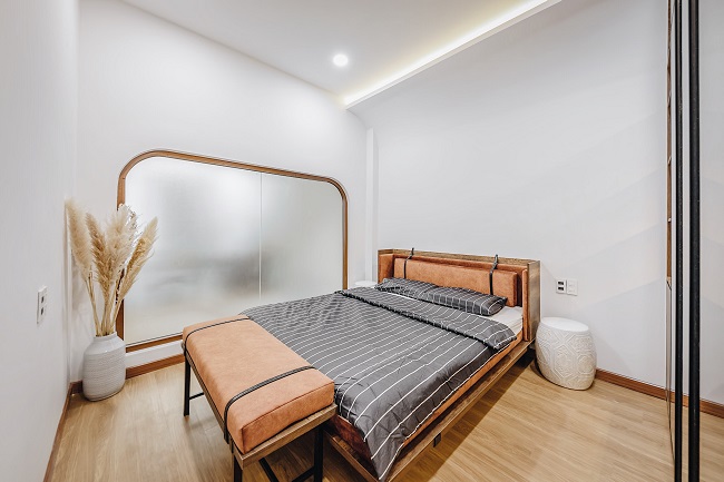 Phòng ngủ ở tầng trệt là không gian nghỉ ngơi của cha mẹ, phù hợp với người lớn tuổi khi sử dụng khu vực sinh hoạt mà không cần di chuyển lên cầu thang. Mảng tường thiết kế bo cong giúp không gian thêm mềm mại, nổi bật.
