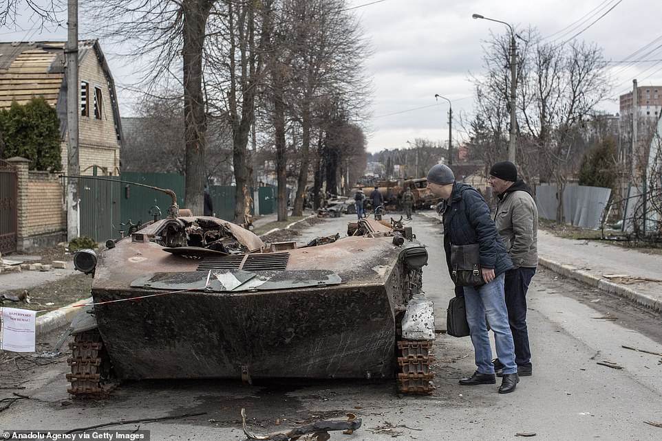Người dân Ukraine đứng bên cạnh xác một xe bọc thép ở thị trấn Bucha, ngoại ô Kiev.
