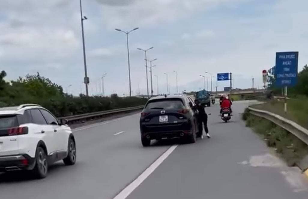 Người phụ nữ đu bám bên hông xe ô tô Mazda đang di chuyển.