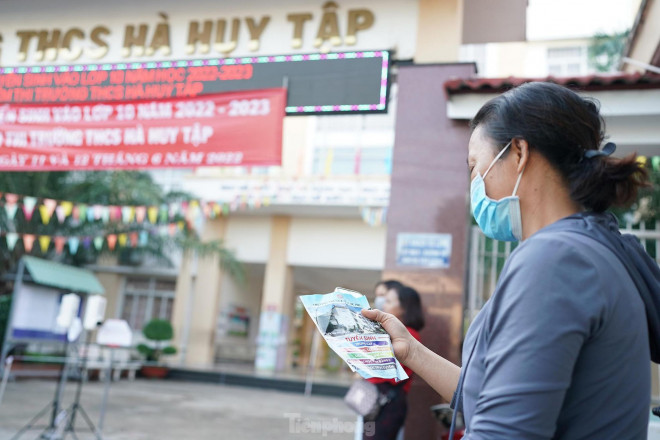 Phía bên ngoài điểm thi, một phụ huynh đợi con và tham khảo thông tin tuyển sinh của một số trường.