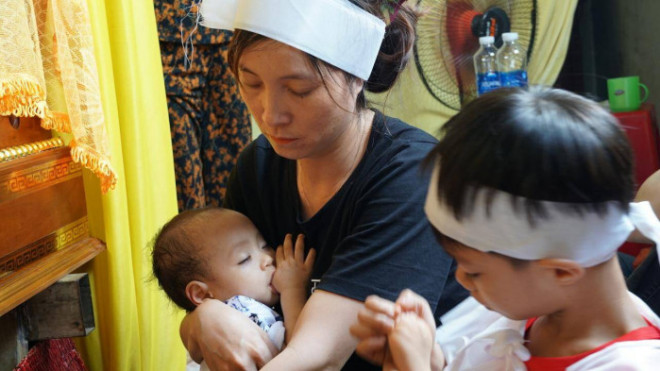 Cháu bé 10 tháng tuổi mồ côi cả cha lẫn mẹ đang ngủ trong lòng người bác ruột. Cháu bé say sưa bú ngón tay.