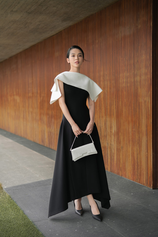 Quỳnh Lương trở nên dịu dàng trong thiết kế váy Martine tối giản với kết cấu cổ đổ và kỹ thuật drape trên vai của Cường Đàm. Để hài hoà với hai màu sắc kinh điển đen - trắng của bộ cánh, Vy của “Đừng làm mẹ cáu” cũng mix giày - túi cùng tone, tạo nên tổng thể thanh lịch.&nbsp;So với cách mix boots đen rất “fashionista” của model lookbook, sự lựa chọn giày cao gót cổ điển của Quỳnh Lương trong set đồ mang đến cảm giác gần gũi với đời thường hơn.&nbsp;