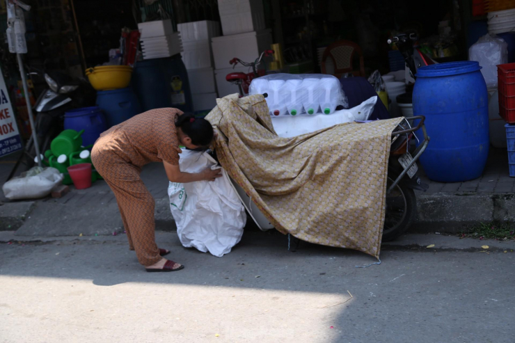 Người phụ nữ lấy bao bì để chống nắng cho xe máy ở khu vực chợ Vinh.