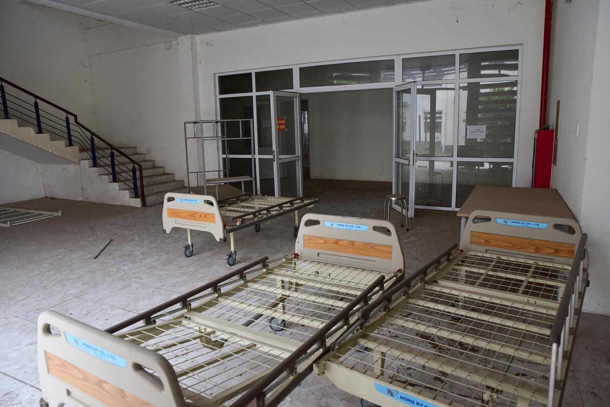 Nhìn từ bên ngoài vào khu nhà, nhiều giường bệnh đặt lộn xộn trước hành lang, sảnh lối vào.