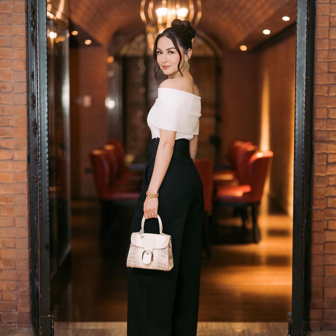 Marian diện outfit đen - trắng. Cô phối áo trễ vai, quần cạp cao Alaïa với túi xách Delvaux và trang sức, đồng hồ hiệu Buccellati.