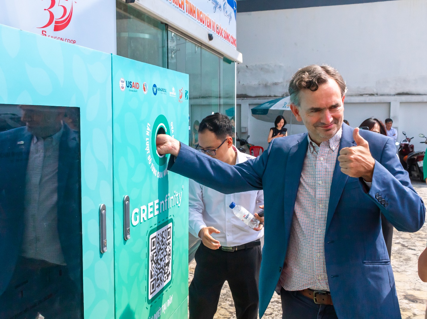 Ông John Harris trải nghiệm quá trình bỏ chai nhựa vào máy thu gom chai nhựa, lon nhôm.