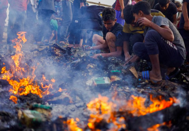Người Palestine tìm lại đồ ăn trong đám cháy sau cuộc không kích của Israel vào khu lều của người di tản. (Ảnh: Reuters)