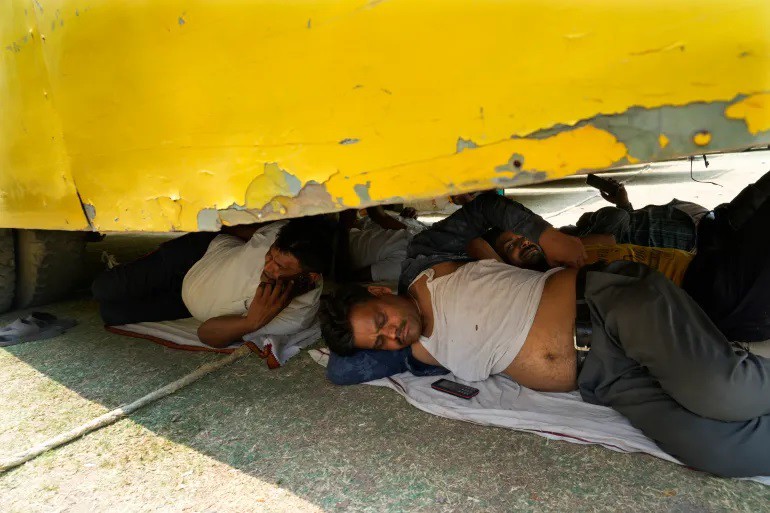 Nhân viên phục vụ bầu cử ở Ấn Độ chui xuống gầm xe bus để tránh nóng (ảnh: Al Jazeera)