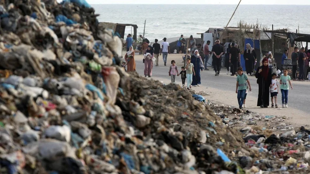 Người dân đi ngang bãi rác ở Deir al Balah (miền trung Gaza) vào tháng 5. Ảnh: ANADOLU AGENCY