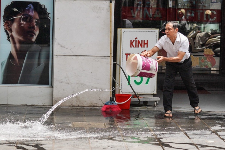 Một người đàn ông đang dội nước tại vỉa hè trước cửa tiệm để giải nhiệt trong cái nắng như rang của Hà Nội.