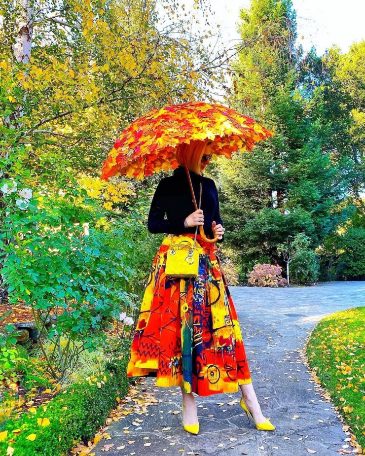 Trong ảnh chụp trong công viên gần nhà ở Mỹ, fashionista kết hợp áo cổ lọ đơn sắc Chanel với chân váy rực rỡ cùng thương hiệu, giày cao gót Christian Louboutin và túi Dior gam vàng đồng điệu. Để tổng thể trông lạ mắt hơn, cô mang dù kết lá vàng, lá đỏ.