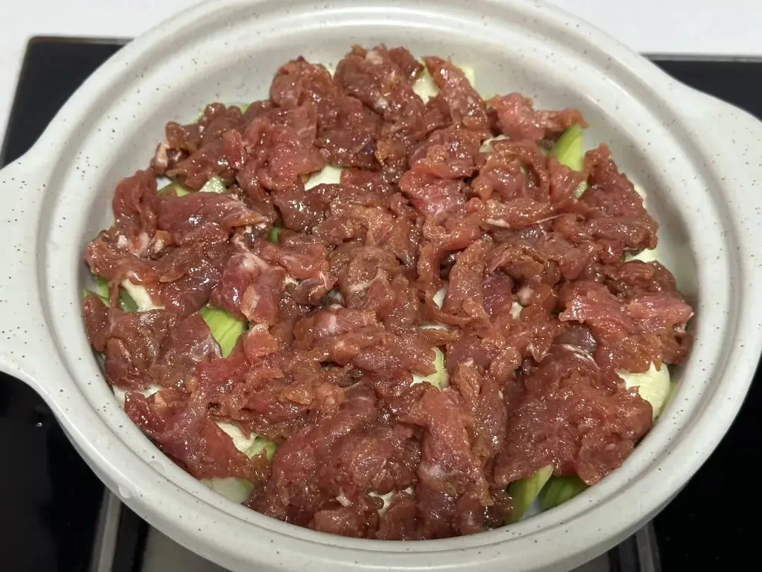 Xếp thịt bò đã ướp đều lên lớp mướp, phủ đều phần nước sốt tỏi lên mặt thịt bò, rưới thêm một bát nhỏ nước&nbsp;quanh mép nồi.