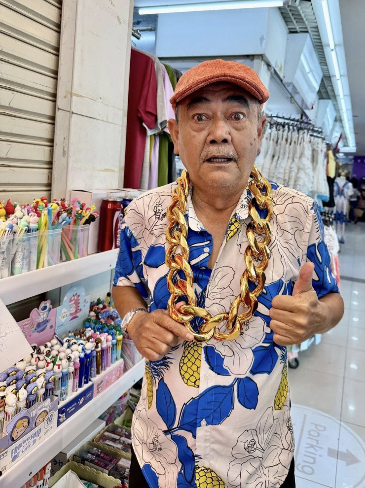 Khi ghé thăm một khu chợ, NSND Việt Anh ngạc nhiên thấy người dân bày bán những sợi dây chuyển bằng vàng giả kích thước khổng lồ. Ông đeo thử và tạo dáng, chụp ảnh hài hước khoe bạn bè, khán giả.