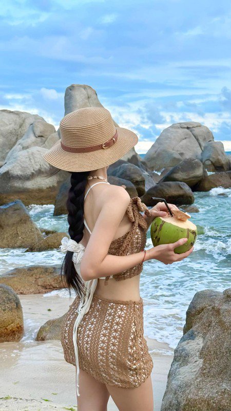 Không thể thiếu chiếc mũ cói rộng vành – phụ kiện “quốc dân” cho mọi cô nàng đi biển, vừa che nắng vừa tăng điểm thời trang. Dây vỏ sò đeo cổ và trái dừa tươi trên tay như hoàn thiện nốt bức tranh “nàng thơ mùa hè”.