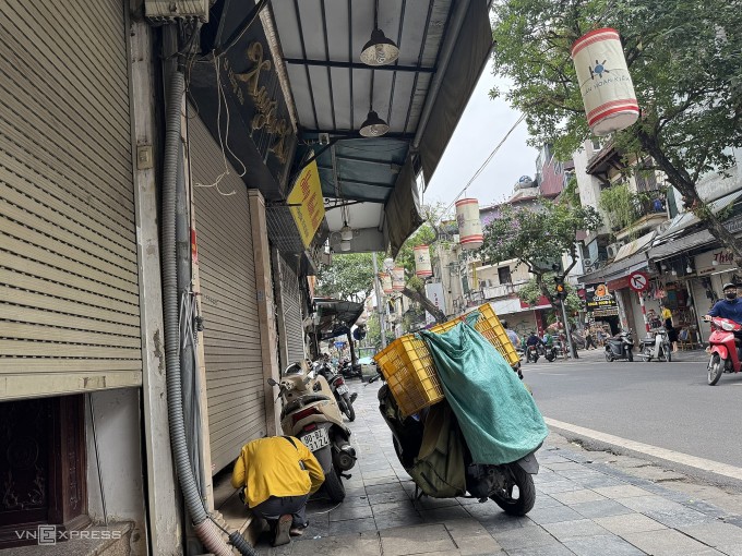 Một shipper phải cúi người sát mặt đất để lấy đơn hàng tại một cửa hàng thời trang trên phố Hàng Đào, quận Hoàn Kiếm, trưa 6/6. Ảnh: Quỳnh Nguyễn