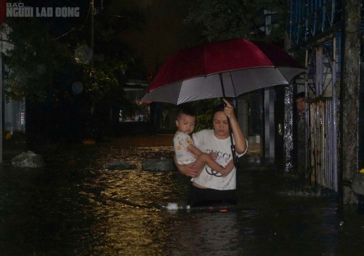 Một người mẹ ôm con, lội nước ra ngoài kiệt Mẹ Suốt trong lúc trời mưa tầm tã.