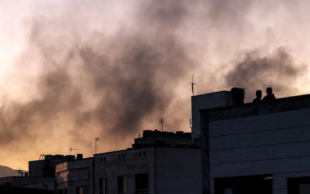Người dân đứng trên mái nhà nhìn các cột khói bốc lên sau một cuộc không kích của Israel tại Tehran ngày 17-6. Ảnh: Atta Kenare/AFP