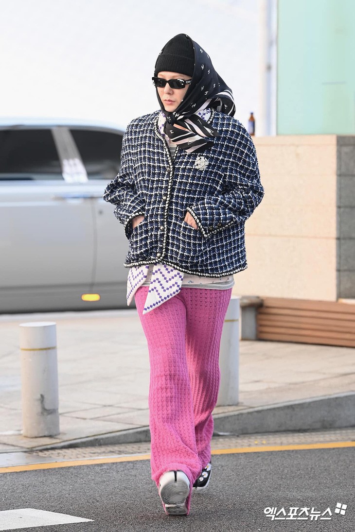 G-Dragon khi bay sang Osaka (Nhật Bản) dự lễ trao giải MAMA, cuối tháng 11/2024. Anh mặc áo dạ tweed phối quần ống loe màu hồng, điểm nhấn là kiểu chít khăn ngoài mũ len.