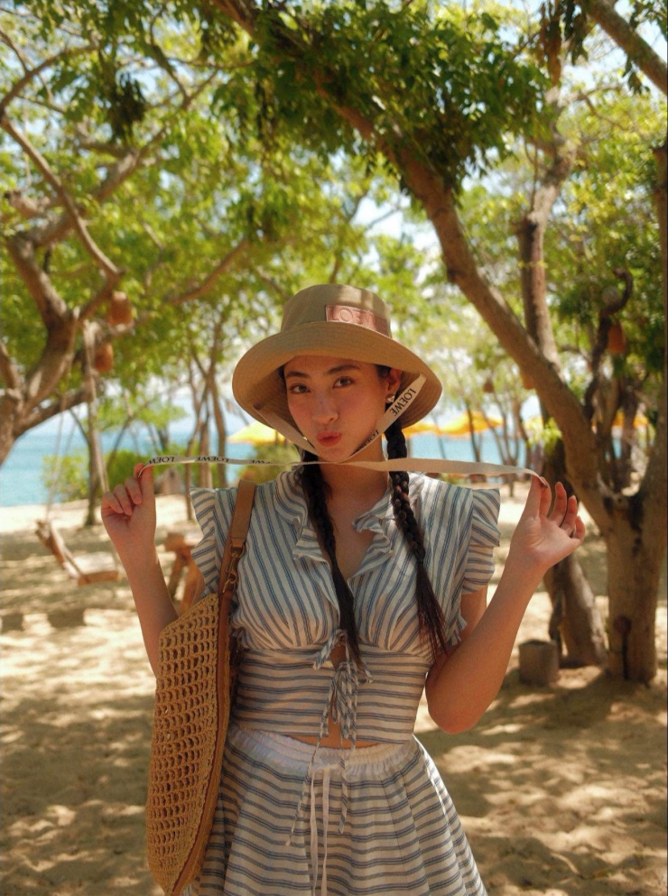 Trong ảnh, người đẹp gốc Cao Bằng diện set đồ kẻ đơn giản, phối phụ kiện mũ và túi cói, không khí biển ngập tràn khung hình.
