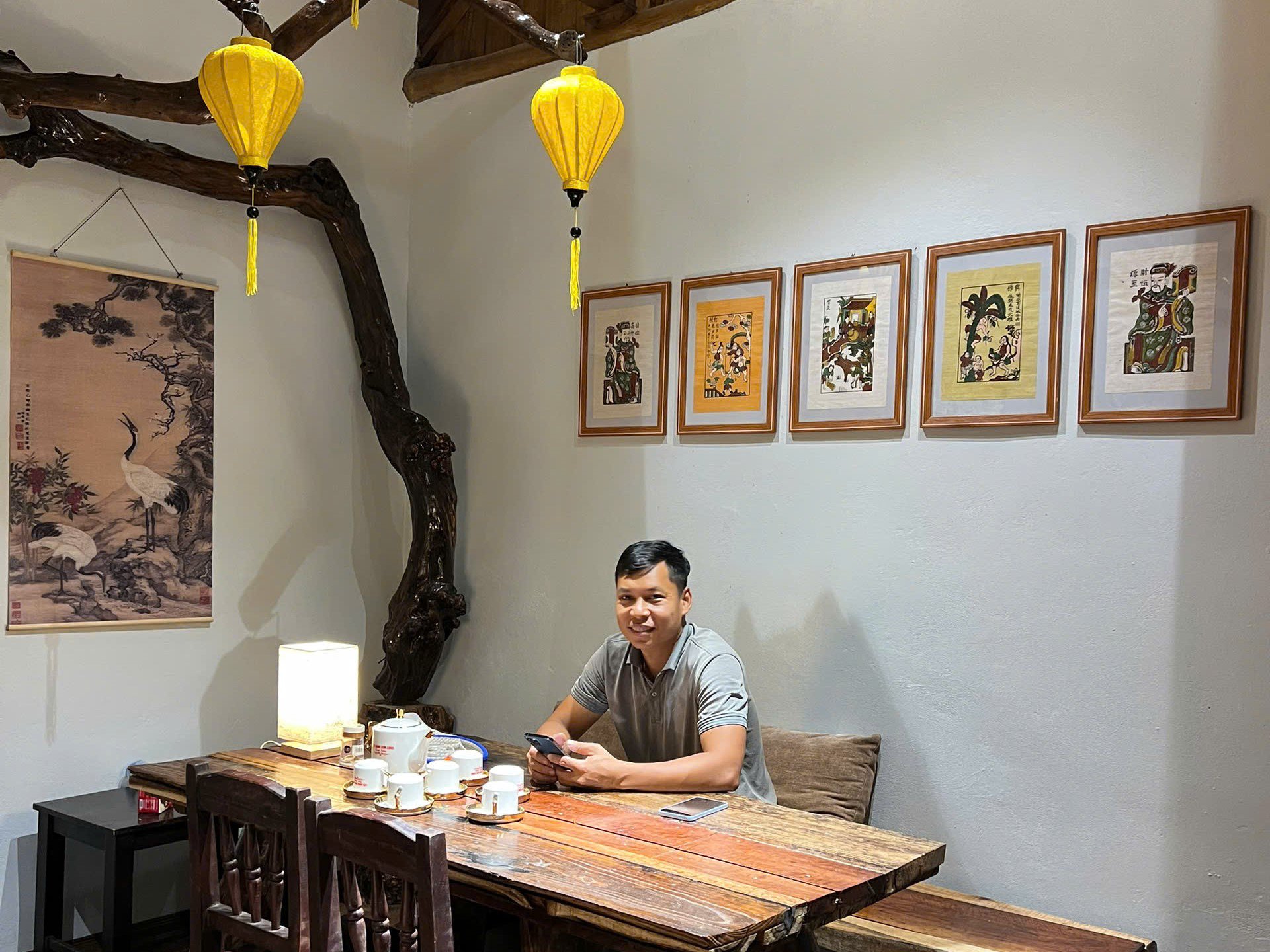 Bàn ghế do anh Sơn tự đóng từ gỗ cũ, cây ổi sau vườn được tận dụng làm góc trang trí cùng với tranh Đông Hồ tạo nên góc ngồi uống trà và tiếp khách.