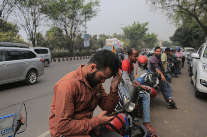 Người dân tại tại thủ đô Dhaka, Bangladesh sử dụng điện thoại "giết" thời gian trong khi chờ mua xăng, cuối tháng 3/2026. Ảnh: Anadolu