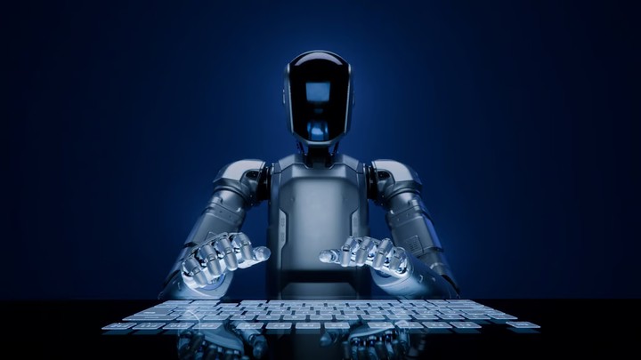 Một robot hình người được trang bị trí tuệ nhân tạo với tấm che mặt bằng kính đang gõ trên bàn phím cảm ứng hiện đại.