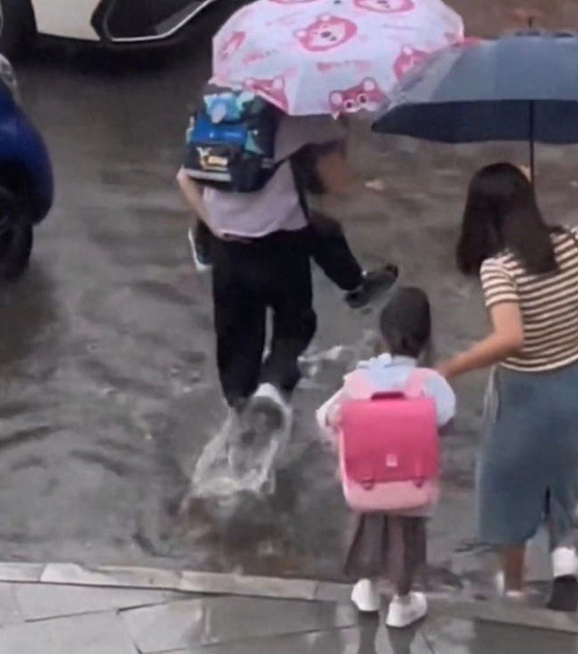 Người mẹ thứ nhất cõng con trai trên lưng để băng qua. Người mẹ thứ hai nắm tay con gái để con tự bước qua. Bé gái mặc áo mưa đứng một mình tự lội qua đoạn đường. Ảnh cắt từ clip