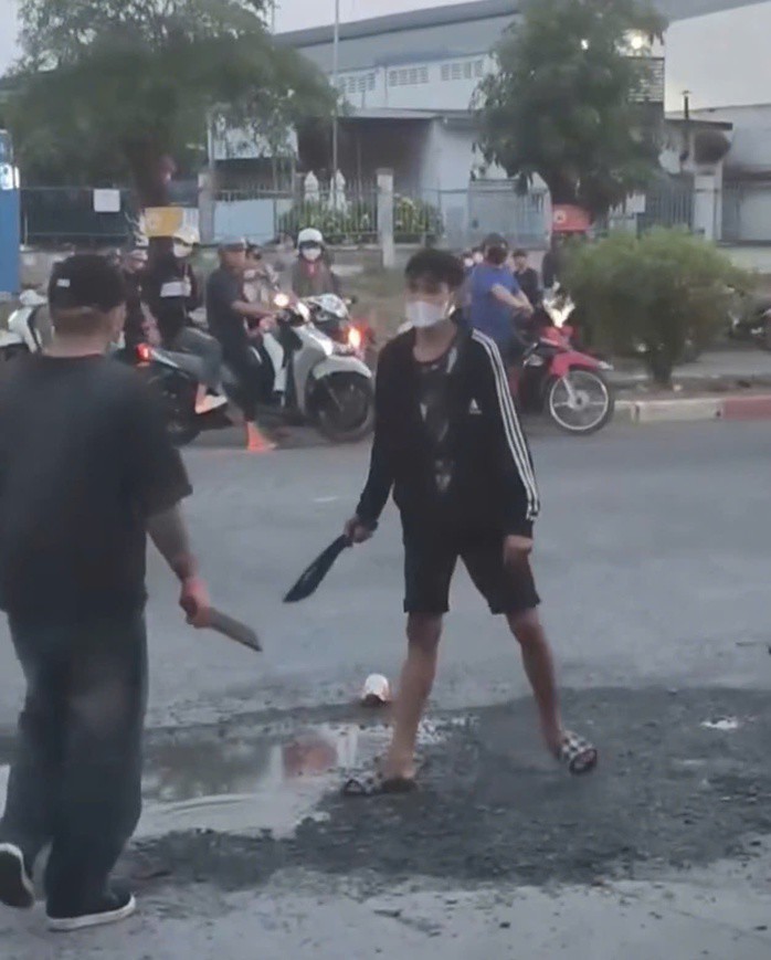 Hai thanh niên cầm hung khí đối đầu trên đường, khiến nhiều công nhân tan ca hoảng sợ. Ảnh cắt từ clip.