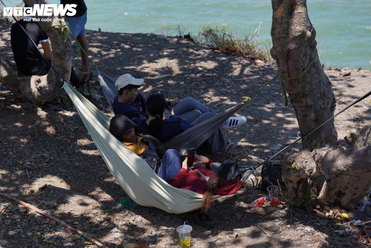 Do thời tiết nắng nóng và khu vực bãi biển thiếu bóng mát, nhiều người chọn mắc võng hoặc trải bạt dưới tán cây để nghỉ ngơi.