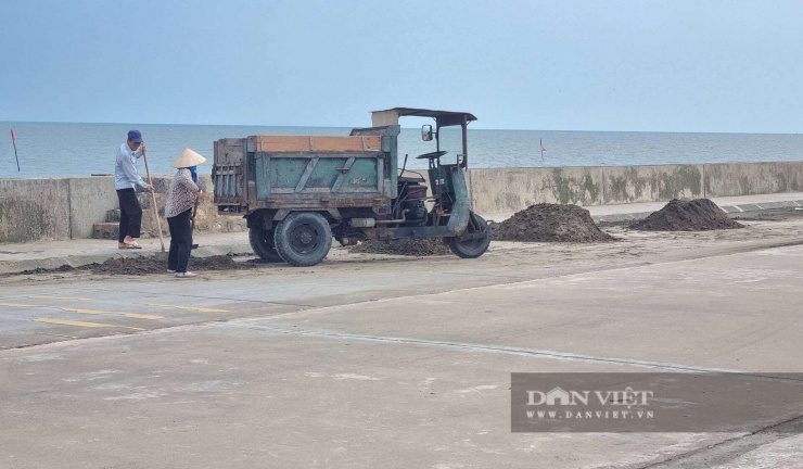 Người dân hốt cát đọng lại do sóng đánh cuốn tràn qua bờ đê. Ảnh: Vũ Thượng