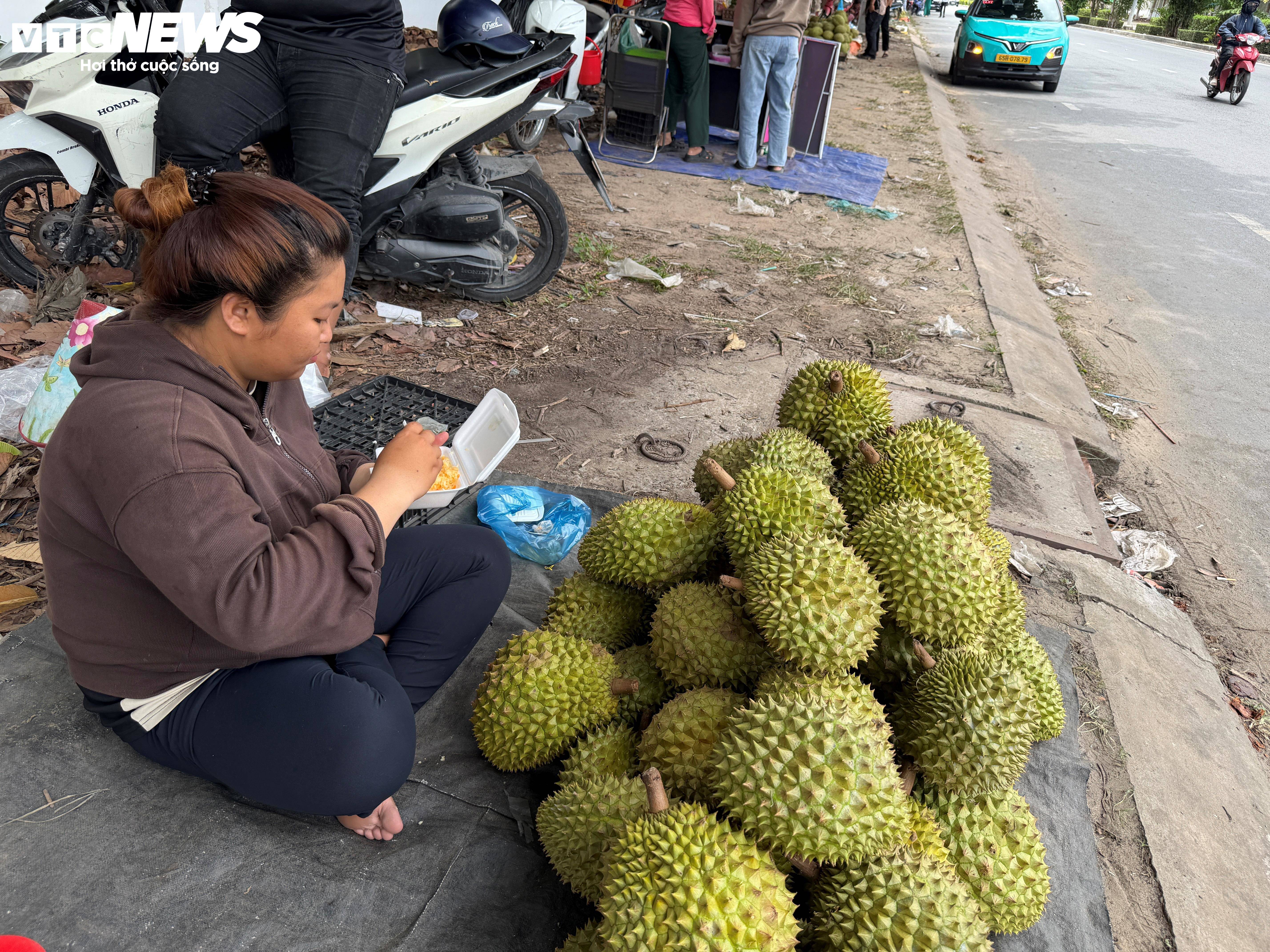 Giữa những giờ ngồi bán sầu riêng dưới nắng nóng, nhiều nhà vườn tranh thủ ăn vội bữa cơm ngay bên lề đường để tiếp tục buôn bán. Với họ, mùa sầu riêng năm nay không chỉ là câu chuyện giá cả lao dốc mà còn là những ngày mưu sinh vất vả, cố gắng bán thêm được bao nhiêu hay bấy nhiêu để bù vào chi phí đầu tư cho cả vụ mùa.