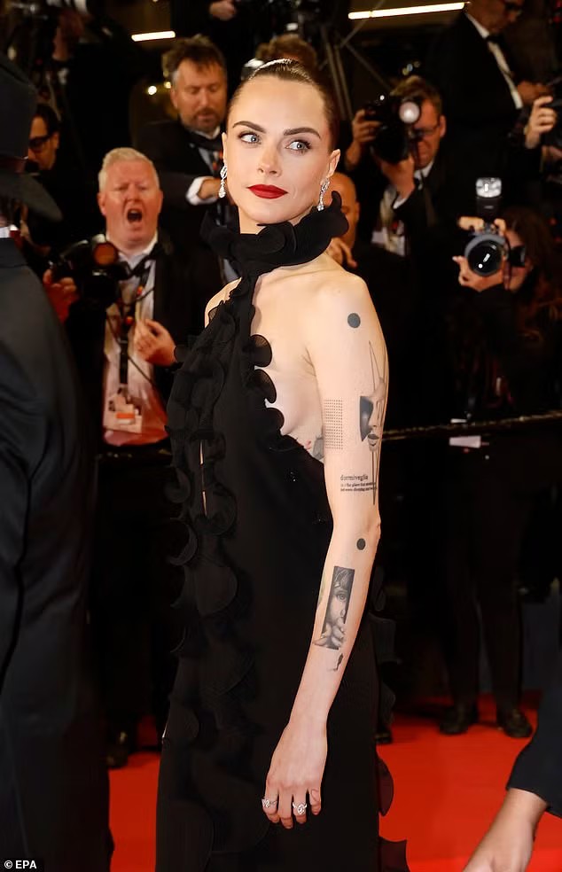 Ngày 15/5 cũng diễn ra buổi ra mắt phim Gentle Monster (hợp tác Đức, Áo và Pháp). Siêu mẫu Anh Cara Delevingne dẫn đầu dàn sao với chiếc váy cổ yếm đen, khoe thân hình mảnh mai và vô số hình xăm trên cánh tay. Cô có màn tương tác đầy thân mật với diễn viên/đạo diễn Jordan Firstman. Hai người đóng vai chính trong Club Kid (2026), bộ phim đầu tay của Jordan. Ảnh: EPA/WireImage