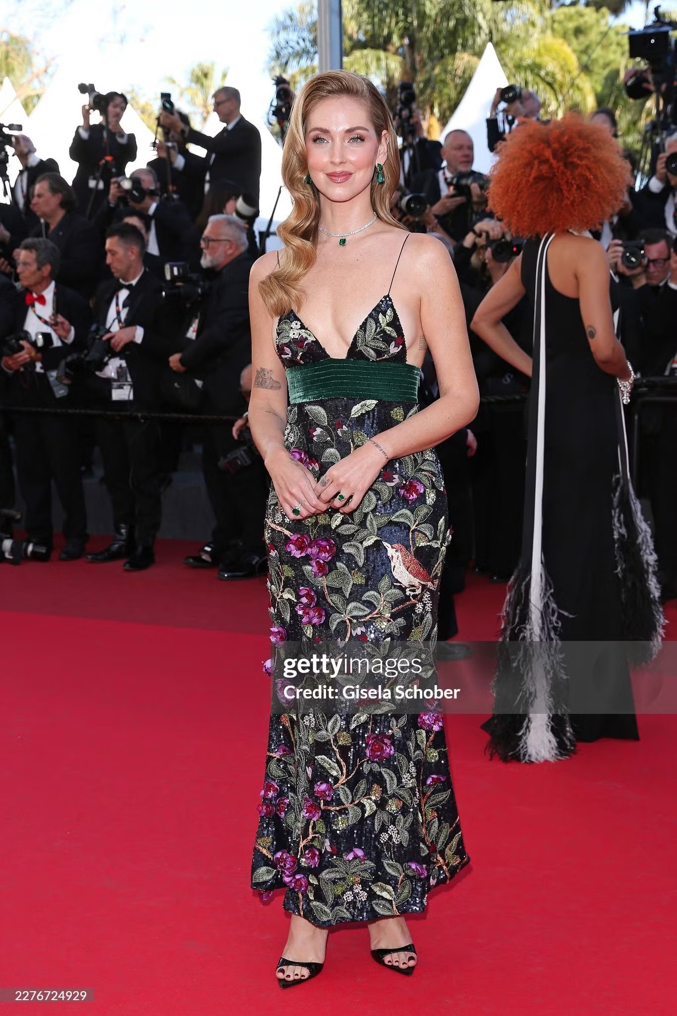 Chiara Ferragni - “bà hoàng influencer” - người Italy trở lại Cannes lần đầu tiên kể từ năm 2021 với bộ váy thanh lịch của Roberto Cavalli, họa tiết thiên nhiên và chi tiết thêu cầu kỳ. Trang sức với sắc xanh lục đồng điệu cùng thắt lưng nhung. Cô hoàn thiện vẻ ngoài bằng kiểu tóc retro uốn sóng phồng kết hợp lớp makeup căng bóng.