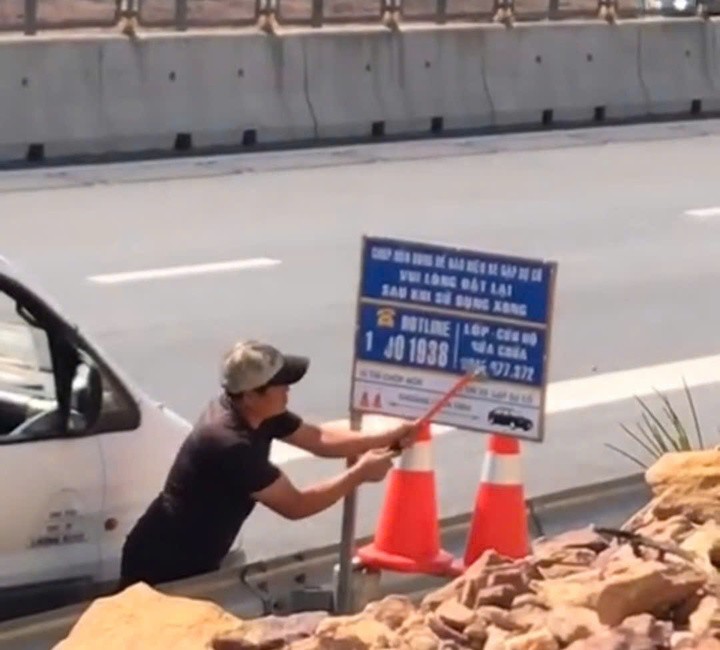 Người đàn ông dùng dao sủi sơn xóa số điện thoại trên bảng thông tin. (Ảnh cắt từ clip)