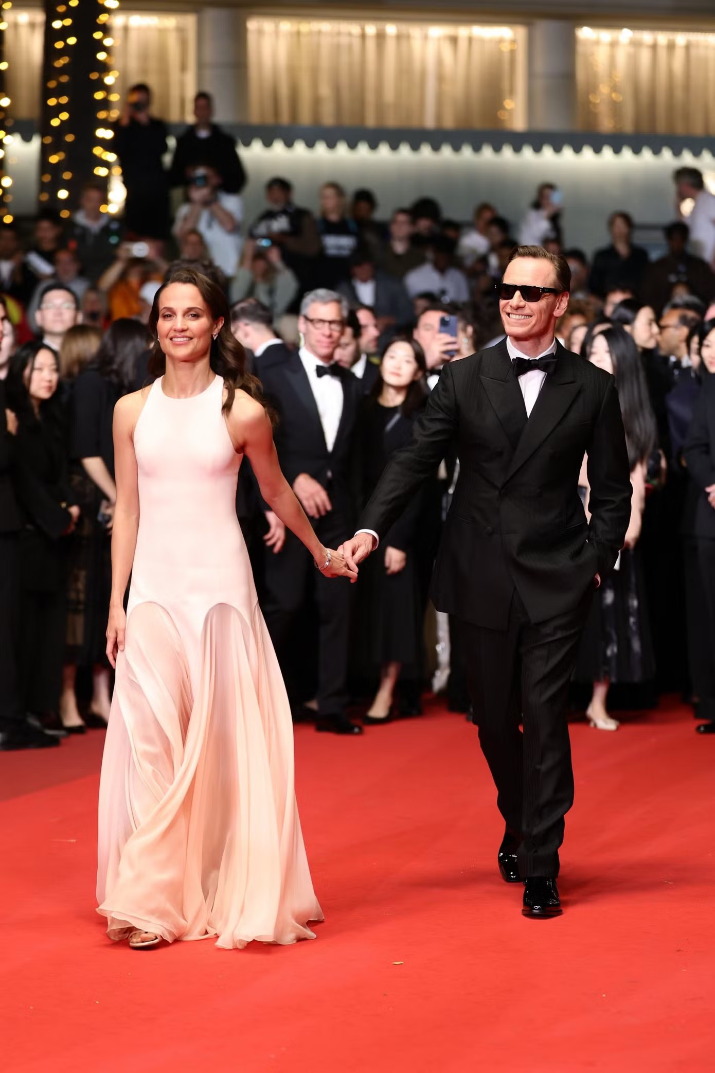 Alicia Vikander và Michael Fassbender - cặp đôi ngoài đời đồng thời là bạn diễn trong phim Hope tay trong tay trên thảm đỏ. Alicia mặc váy hồng nhạt dáng ôm với chân váy cấu trúc hình vòm, còn Michael chọn tuxedo cổ điển kết hợp kính râm và nơ đen.