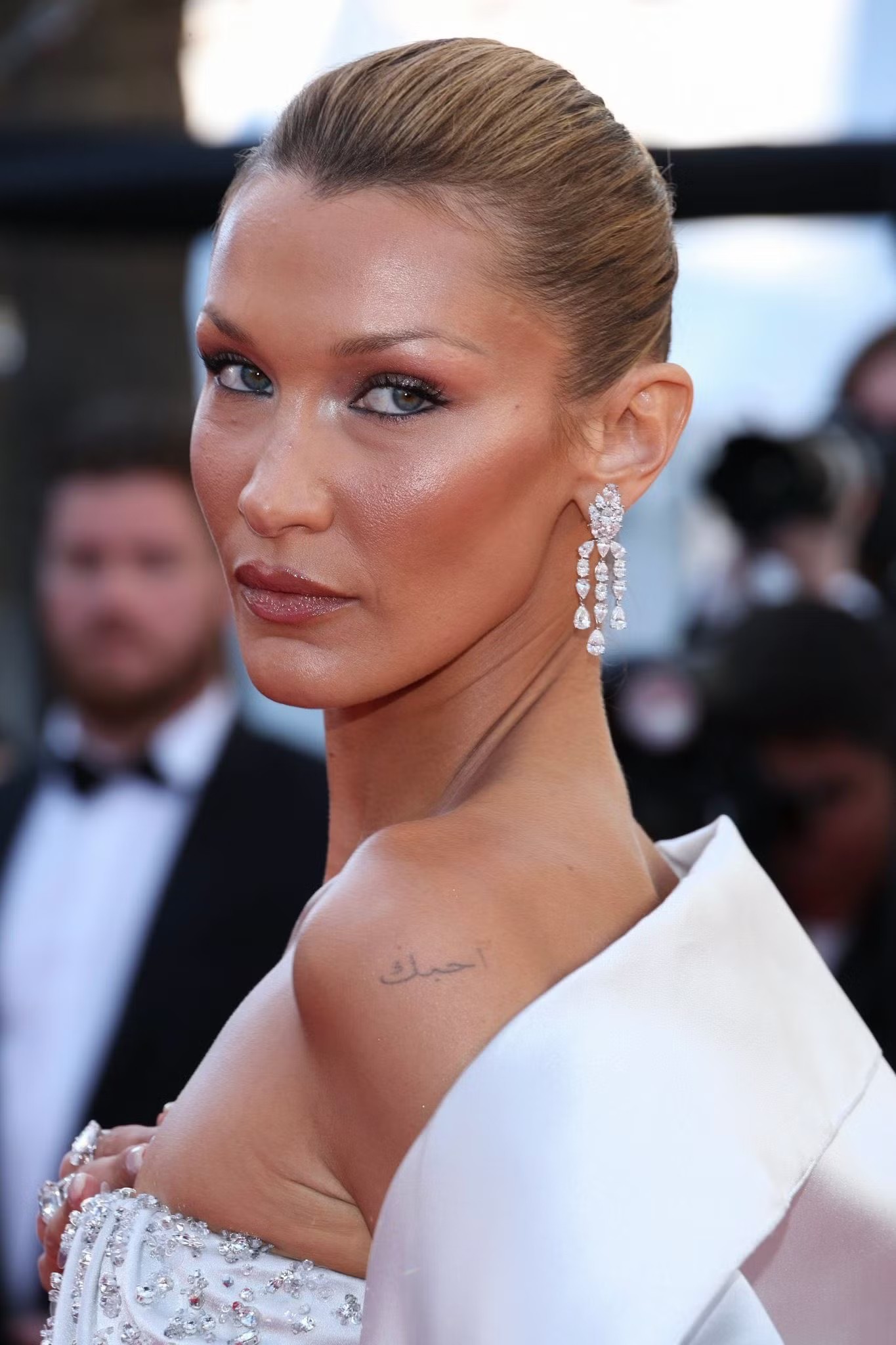 Siêu mẫu Bella Hadid chọn kiểu tóc búi cao kiểu diva cổ điển, làn da rám nắng nhẹ cùng bộ váy Prada may đo riêng. Thiết kế corset được đính pha lê ở phần cổ tim, kết hợp cùng trang sức Chopard. Bella tiếp tục chứng minh sức hút tại Cannes khi xuất hiện cùng em trai Anwar Hadid.
